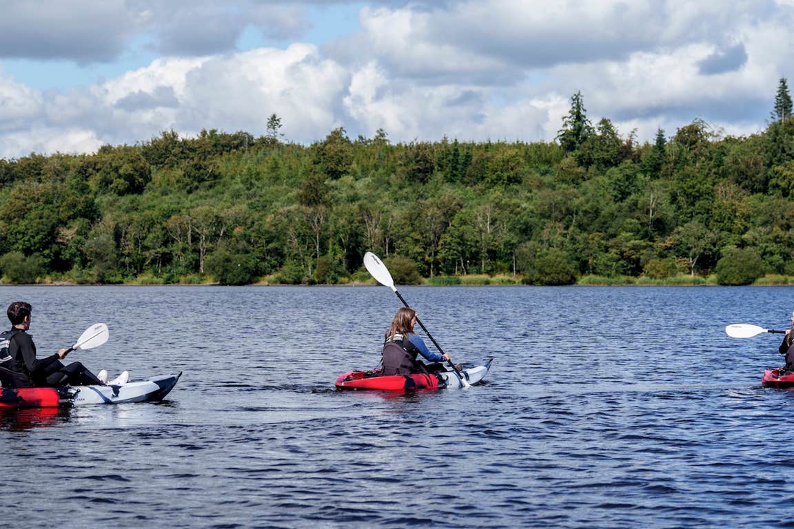 Three people in red kayaks on the open water at the Castleblayney Outdoor Adventure Centre.