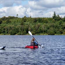 Three people in red kayaks on the open water at the Castleblayney Outdoor Adventure Centre.