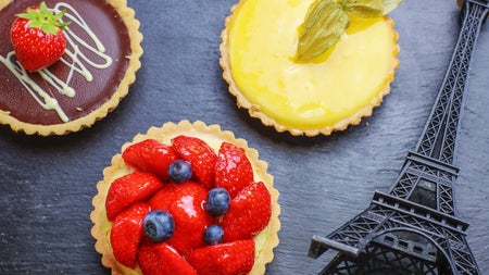 Three tartlets with fruit on a table with a model of the Eiffel Tower beside them