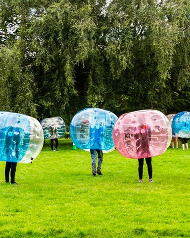 A group of people wearing large plastic bubbles kicking around a football