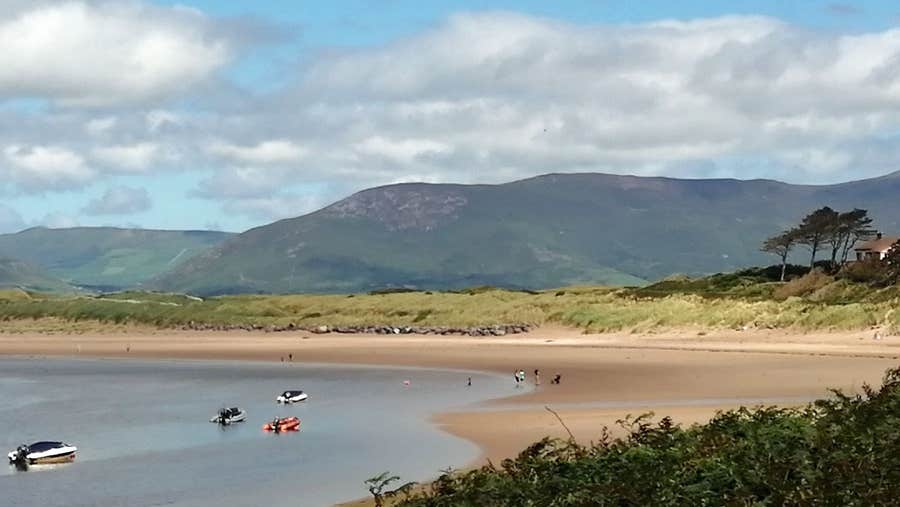 A view of the sandy Dooks Beach with some boats in the water and people walking on the beach