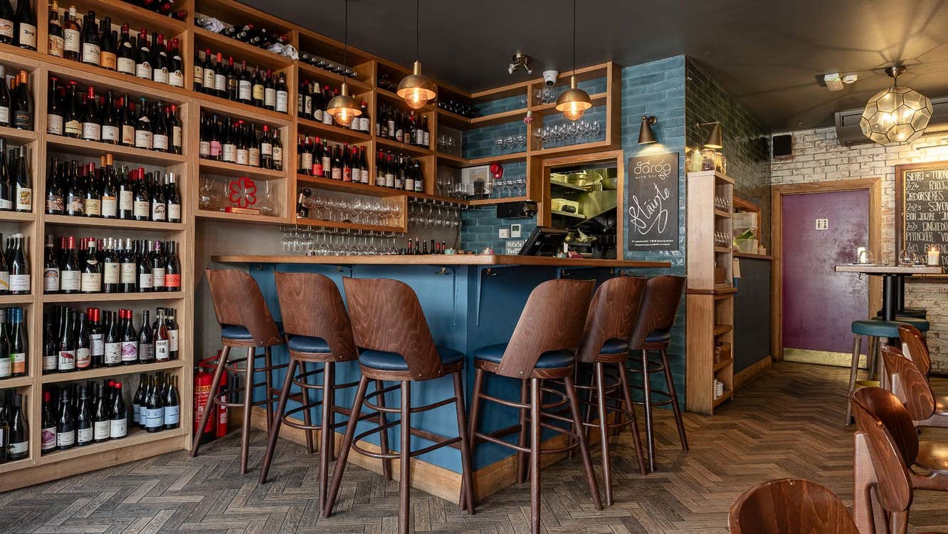 A corner bar counter with a floor to ceiling wall of wine bottles