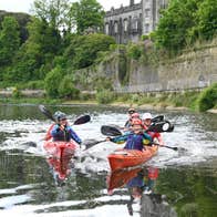 A group of people on the River Nore beneath Kilkenny Castle in double kayaks