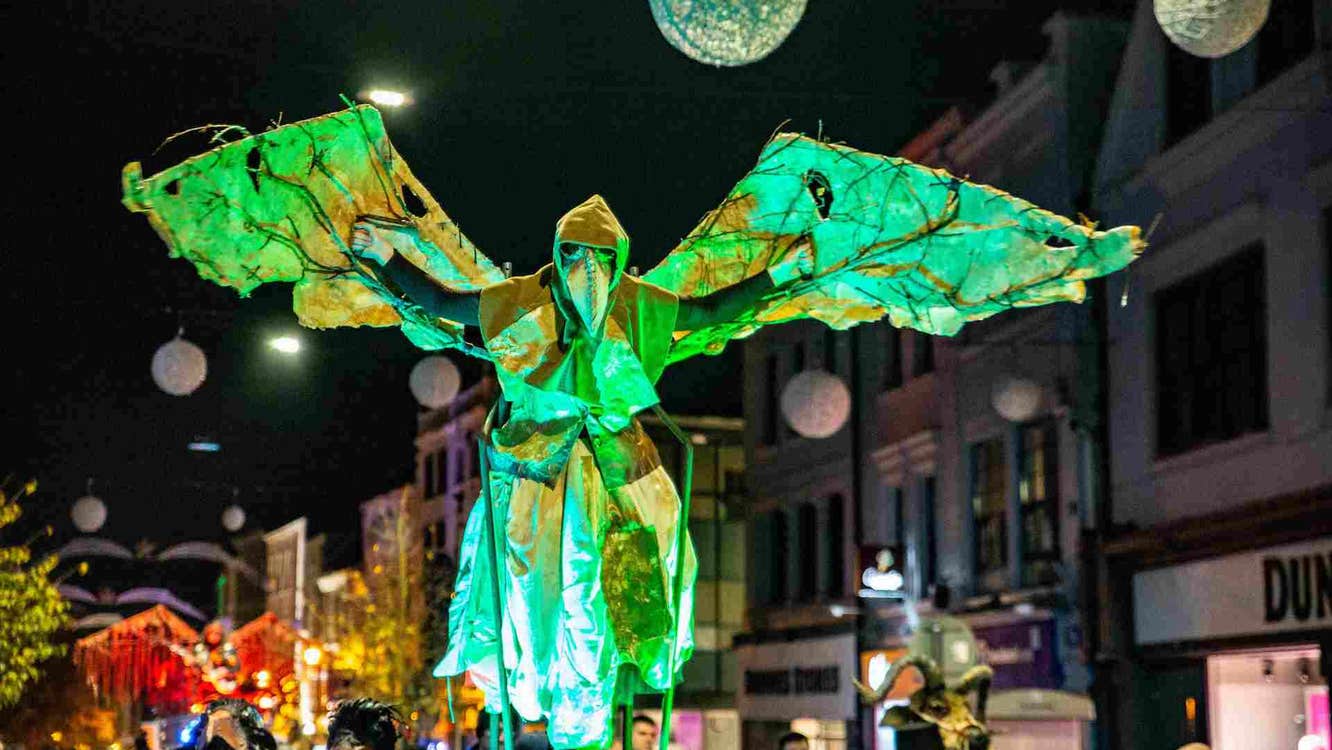 Samhain with Waterford Spraoi. At night in a street parade, a large, green winged costume is above the crowd.