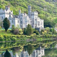 Exterior of a large manor house overlooking a lake with a mountain in the background
