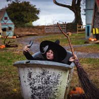 A person with large black hat and broom is in a large grey container taking a selfie.