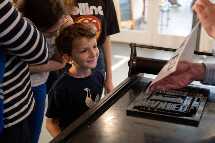 A young boy with his parents behind him looks over a hand rolling proofing press as the guide demonstrates how it works