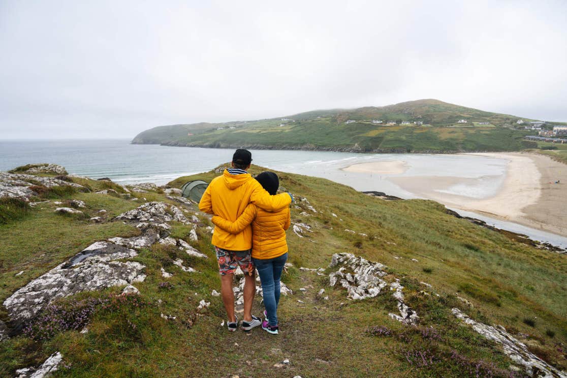 Two people embracing as they look out over the water and beach at Barley Cove in Cork.