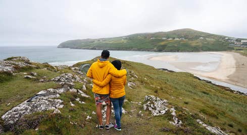 Two people embracing as they look out over the water and beach at Barley Cove in Cork.