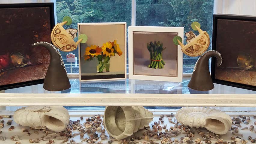 Four small paintings on top of a display case which has three large white sea shells