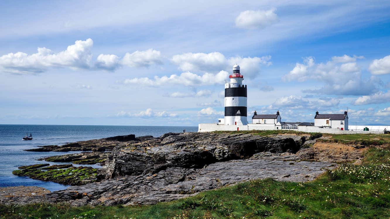 Hook Head Lighthouse beside the sea in Wexford surrounded by rocks and grass.