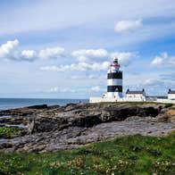 Hook Head Lighthouse beside the sea in Wexford surrounded by rocks and grass.