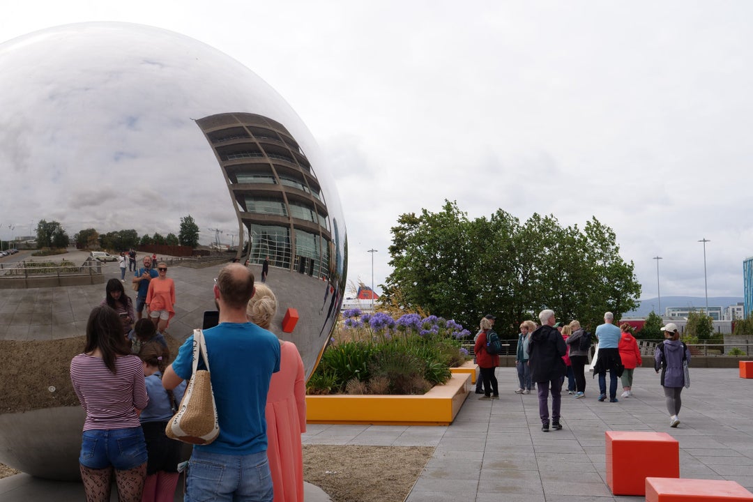 Group of people looking at their reflection in a large silver ball