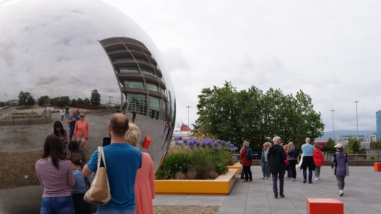 Group of people looking at their reflection in a large silver ball