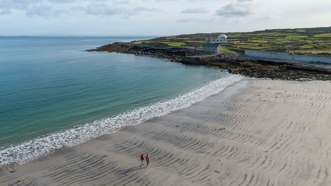 Two people walking own an empty Kilmurvey Beach Aran Islands, Galway