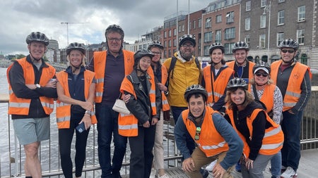 Group of people in orange high visibility vests posing for a picture on a bridge