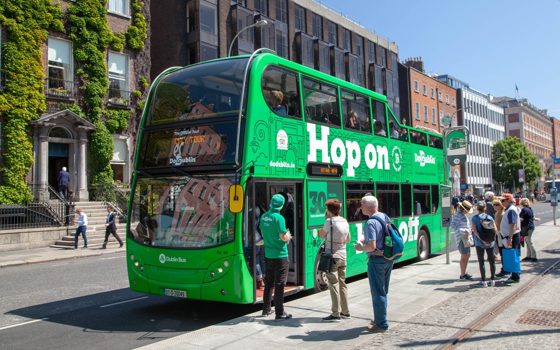 A large green double decker bus with people queueing to get on it