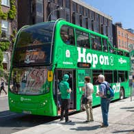 A large green double decker bus with people queueing to get on it
