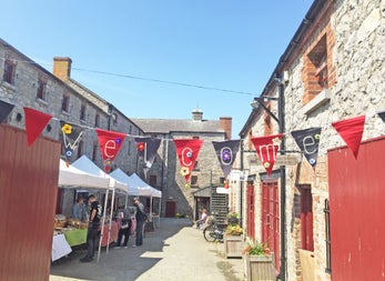 Skerries Mills Farmers Market stalls in a lane next to old stone buildings and a welcome sign