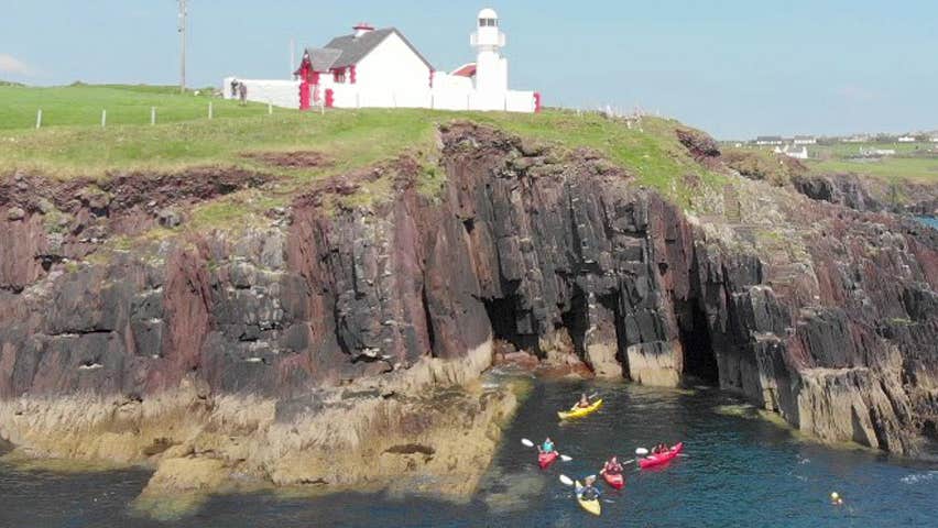 Irish Adventures kayakers in the sea below cliffs and a lighthouse