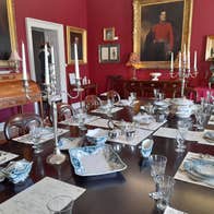 Large dining table set for service in a room with red walls and painting hanging on them