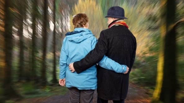 Aisteoirí an Bhaile Mhaigh Cuilinn Double Bill - 2 people viewed from behind with an arm around each other's waist with a blurry forest background.