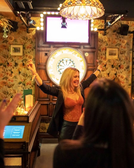 Flight Club Dublin woman celebrating in front of an electric dart board with friends