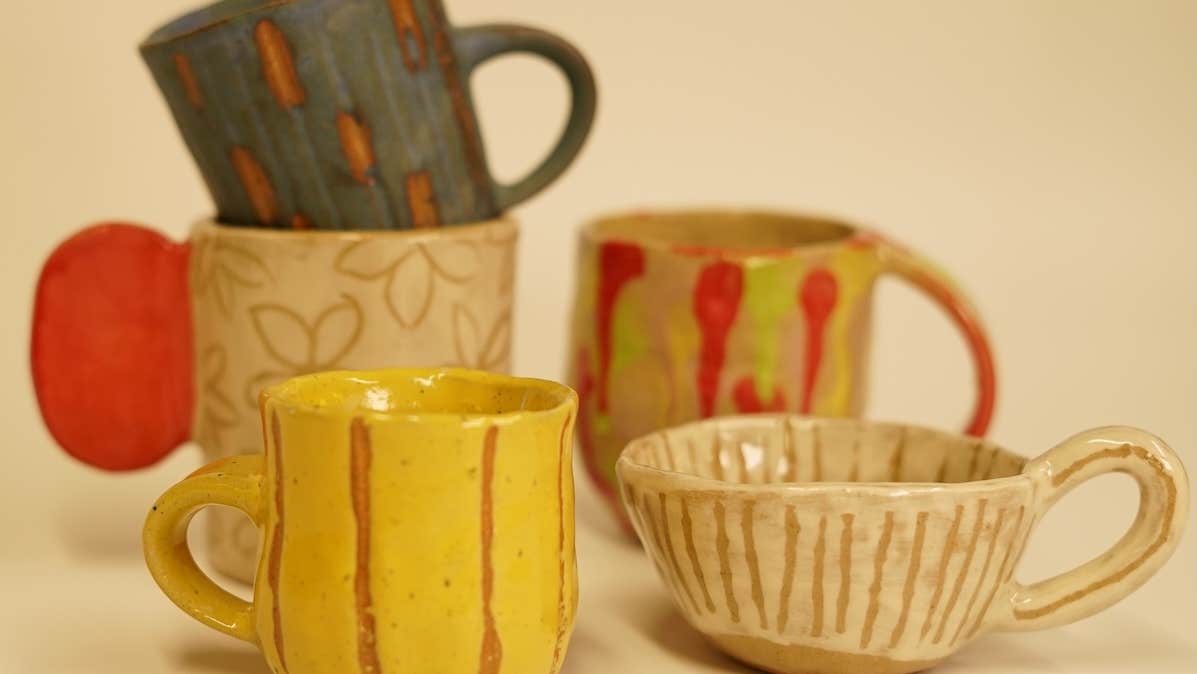 A group of 5 small, rustic handmade mugs in shades of yellow, beige, red and dark green.
