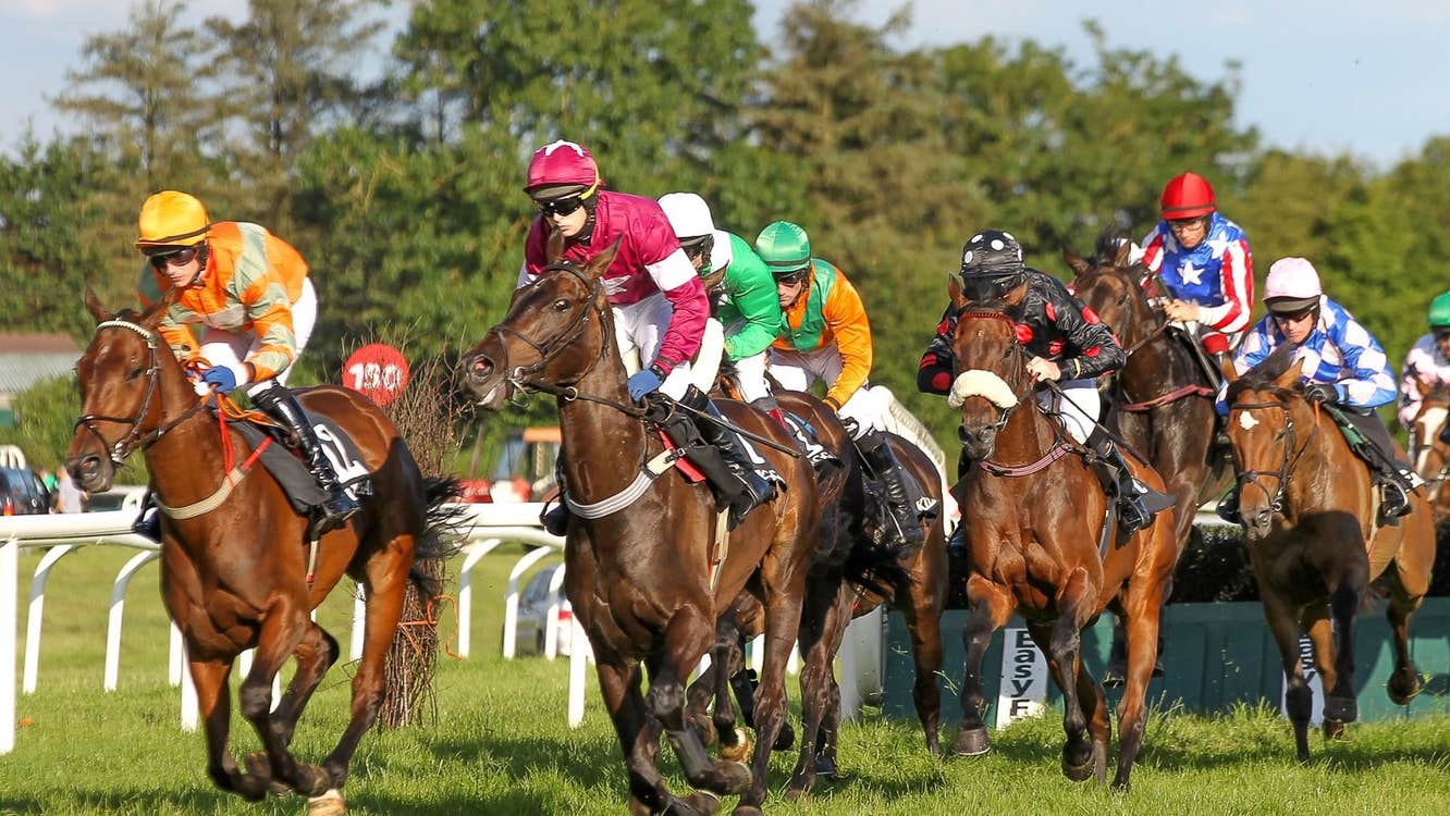 A group of brown horses with jockeys running along a race course.