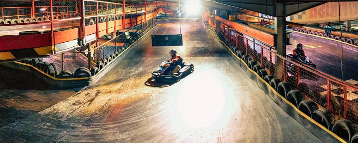 A lone driver taking a bend on an indoor karting track