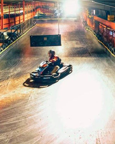 A lone driver taking a bend on an indoor karting track