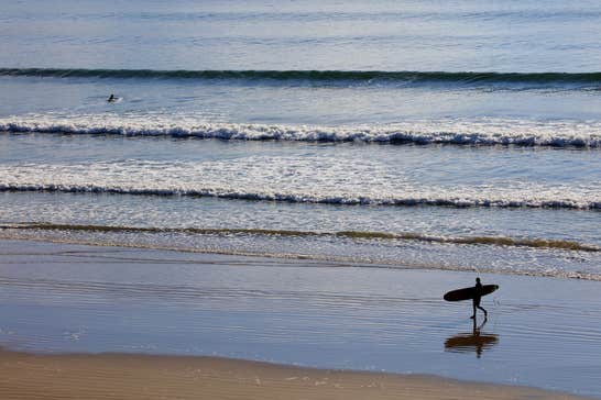A surfer walking along Inch Strand in County Kerry with their surfboard.