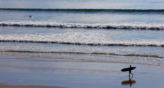 A surfer walking along Inch Strand in County Kerry with their surfboard.