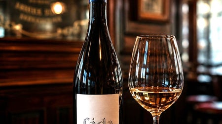 A bottle and glass of white wine called Fada on a dark wood coloured table