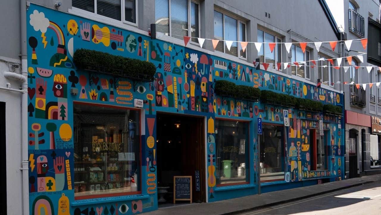 Outside a colourfully painted coffee shop on a street with red and white bunting