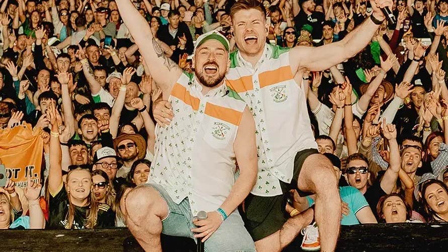 2 men kneeling down, shouting and waving arms in the air with a large waving crowd behind them