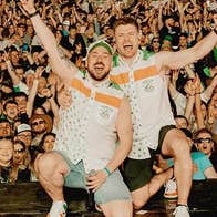 2 men kneeling down, shouting and waving arms in the air with a large waving crowd behind them