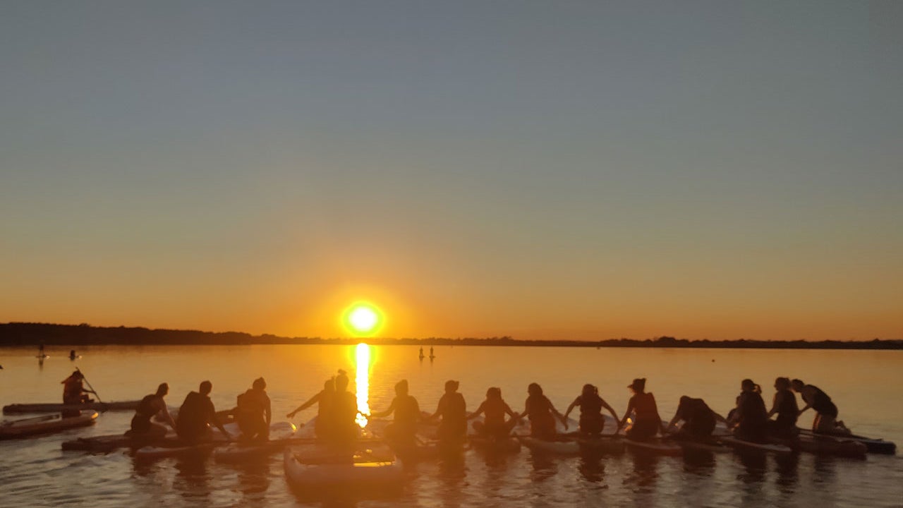 A group out on the paddleboard tour with the sun going down in the back ground