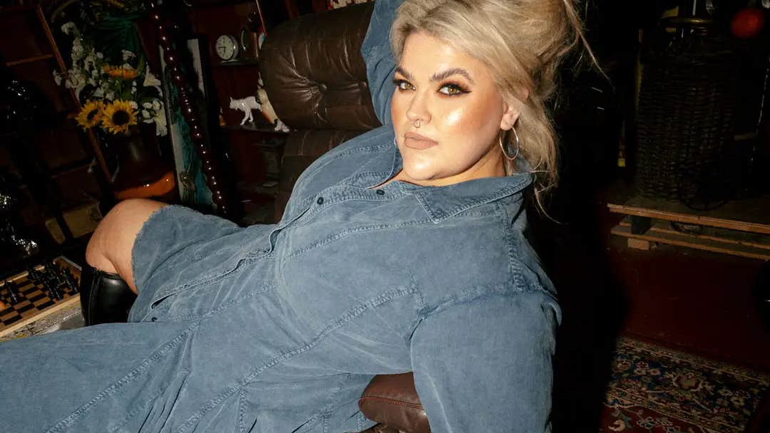 A woman in a blue denim dress is laying draped across a chair