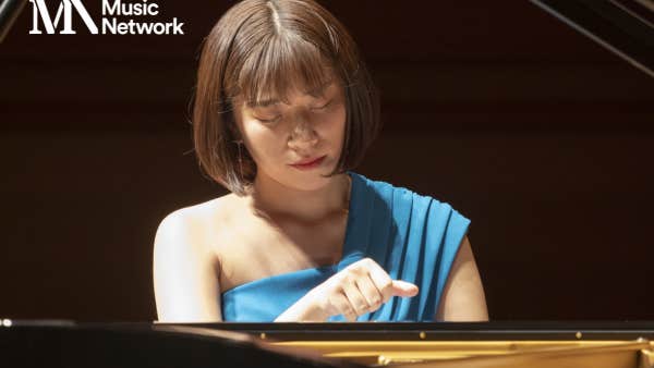 A woman seated at the keyboard of a piano looking down.
