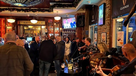 Interior of pub with a man playing guitar and a woman playing the banjo and people standing near bar counter
