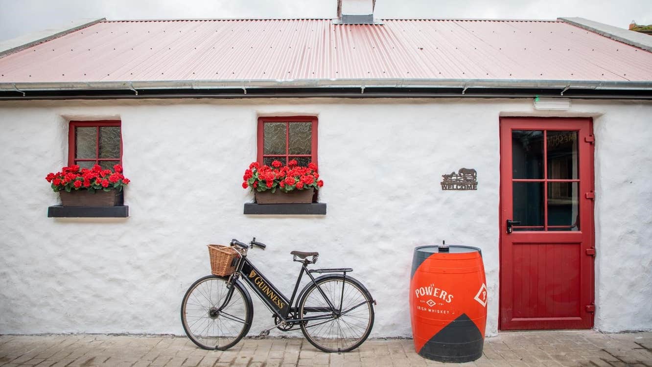 White cottage with red windows and door and a bike and barrel outside