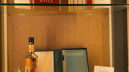 Display shelves containing books, bottle & glass, a pair of glasses and other small items.