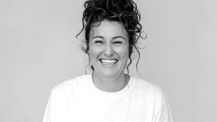 A broadly smiling woman with plain top and background.