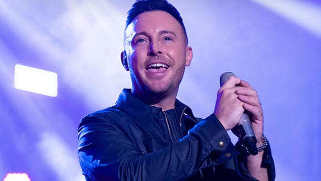 A smiling man holding a mic on a lit stage