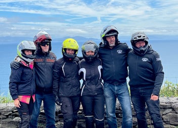 A group of bikers with their helmets on standing side by side at a coastal view