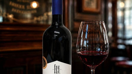 A bottle and glass of wine called Lusca on a dark wood coloured table top