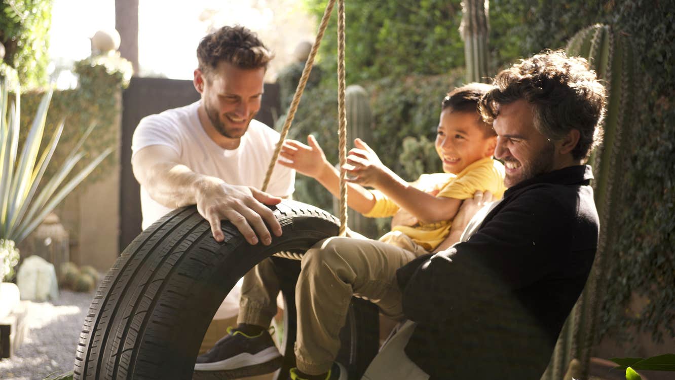 Two men and a boy are playing with a tyre swing.