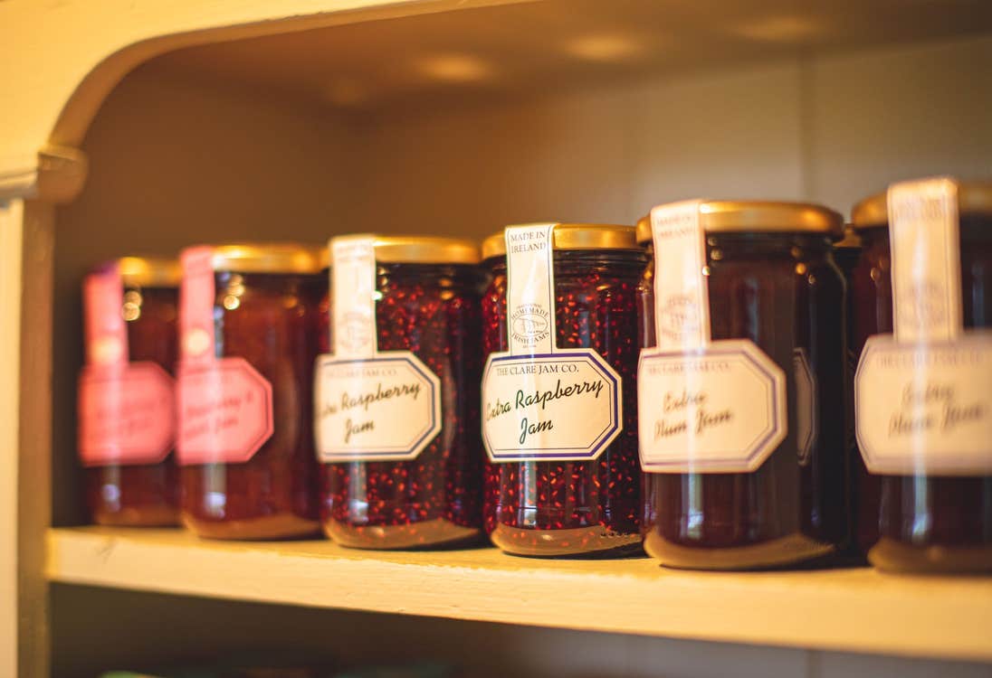 Six jam jars on a shelf with white and pink labels