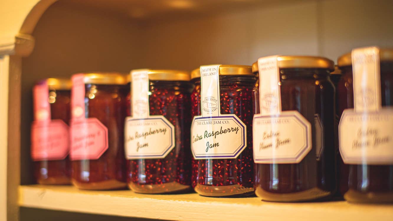 Six jam jars on a shelf with white and pink labels